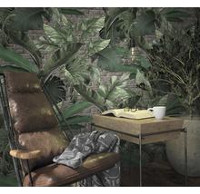 Wohnzimmerszene mit Sessel, Tisch, Buch, Tasse und Pflanzen vor einer Tapete mit Blattmuster