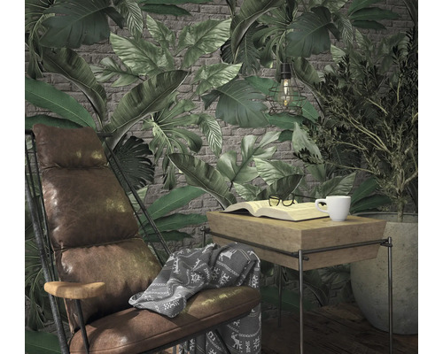 Wohnzimmerszene mit Sessel, Tisch, Buch, Tasse und Pflanzen vor einer Tapete mit Blattmuster