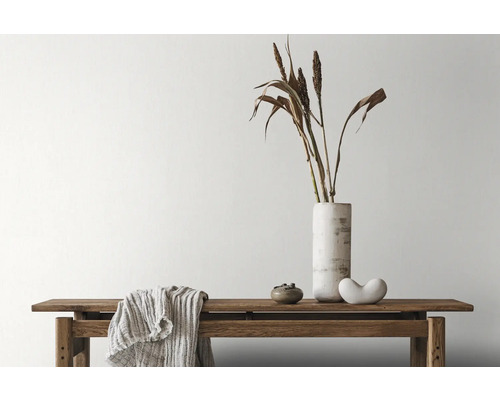 Dekorative Anordnung mit Bank, Vase, Ziergras und Textilien im Innenraum.