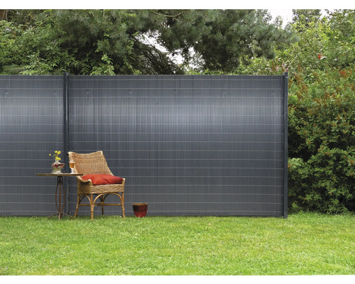 Gartenszene mit Sichtschutzzaun, Rattansessel und kleinem Tisch auf einer Rasenfläche