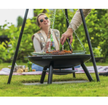 Person grillt Fleisch auf einem Dreibein-Grill im Garten