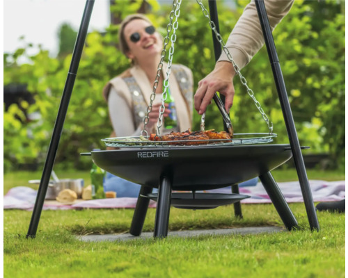 Person grillt Fleisch auf einem Dreibein-Grill im Garten
