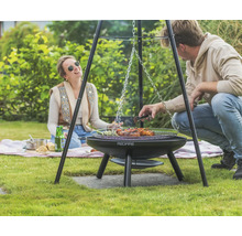 Szene mit einem Dreibein-Grill von Redfire im Garten mit zwei Personen beim Grillen von Speisen.