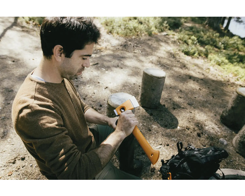 Mann sitzt im Wald und hält eine Axt.