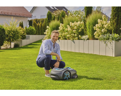 Mann hockt neben einem Mähroboter im Garten