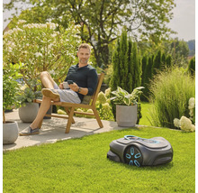 Ein Mann entspannt im Garten mit einem Rasenmähroboter im Vordergrund