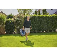 Ein Mann trägt einen Gardena Mähroboter über einen Rasen