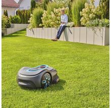 Gardena Mähroboter im Garten mit Mann, der sich an einer Gartenmauer ausruht