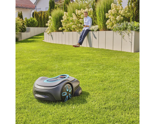 Gardena Mähroboter im Garten mit Mann, der sich an einer Gartenmauer ausruht