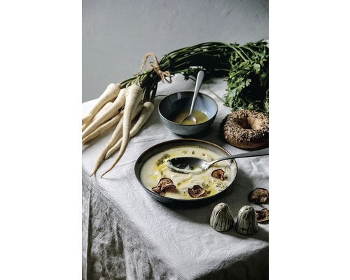 Stillleben mit Pastinakensuppe, Petersilie, Bagel und Gewürzstreuern auf einem Tisch