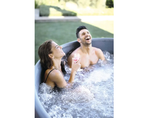 Zwei Personen entspannen lachend in einem Badezuber im Garten
