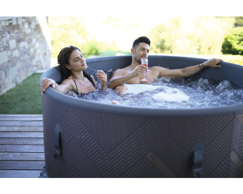 Ein Paar entspannt in einem aufblasbaren Whirlpool im Freien mit Getränken.