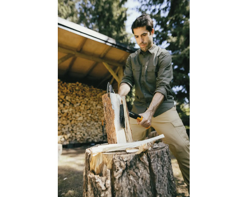 Mann spaltet Holz mit einer Spaltaxt auf einem Hackklotz im Freien.