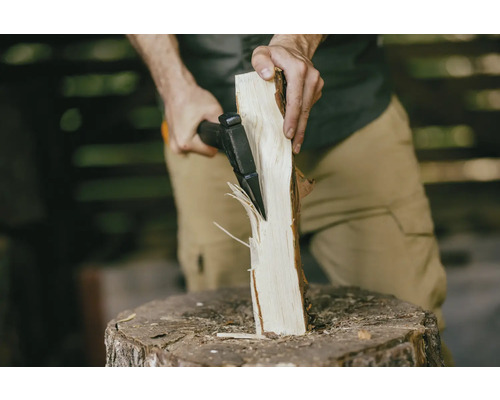 Eine Person spaltet mit einer Axt ein Stück Holz auf einem Hackklotz.