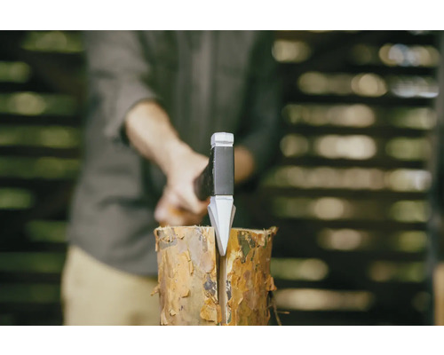 Mann spaltet Holzscheit mit einer Spaltaxt.