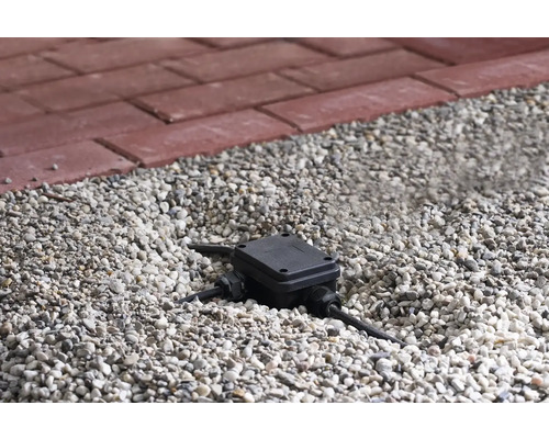 Abzweigdose im Kiesbett mit rotem Pflasterstein im Hintergrund