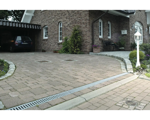 Einfahrt mit Pflastersteinen, Entwässerungsrinne und Haus im Hintergrund