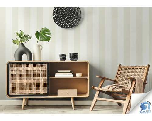 Wohnzimmerszene mit Kommode, Dekoration und Rattansessel vor einer gestreiften Wand