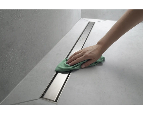 Eine Person reinigt eine Duschrinne mit einem Tuch