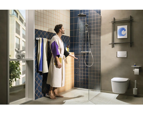 Modernes Badezimmer mit Dusche, Toilette und Waschtisch sowie einem Mann im Bademantel, der die Temperatur des Duschwassers überprüft.