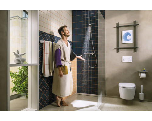 Mann unter der Dusche in einem Badezimmer mit Toilette und Handtüchern.