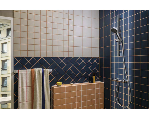 Badezimmer mit Fliesen in verschiedenen Farben, Handtüchern und Duschkopf