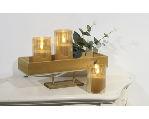 Dekorative LED-Kerzen in Glasbehältern auf einem Holztablett mit Pflanzen auf einem Tisch