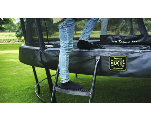 Person steigt auf eine Leiter zu einem schwarzen Gartentrampolin mit Sicherheitsnetz.