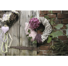 Dekorative Kränze hängen an einer Holztür und einer Ziegelwand, geschmückt mit Blumen, Herzen und Pflanzen.