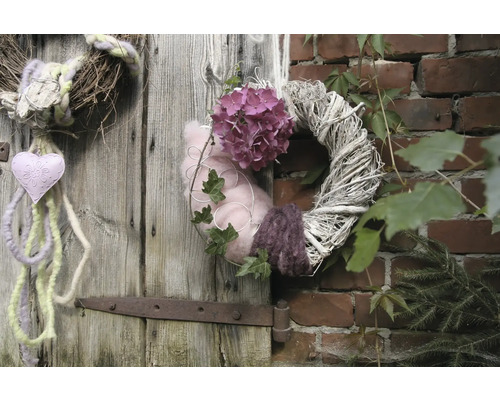 Dekorative Kränze hängen an einer Holztür und einer Ziegelwand, geschmückt mit Blumen, Herzen und Pflanzen.