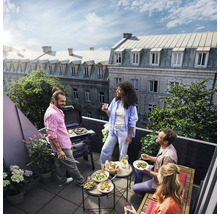 Gruppe von Personen grillt auf einem Balkon mit Grill, Beistelltischen, Salatschüsseln und Sitzgelegenheiten.