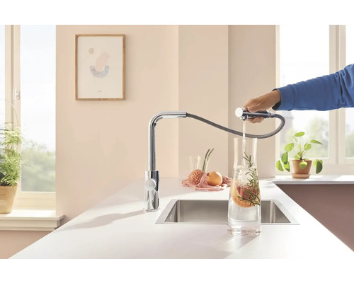 Küchenszene mit verchromtem Wasserhahn und Brauseschlauch, der Wasser in ein Glas füllt