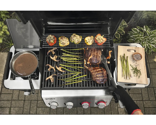 Gasgrill mit Grillgut wie Steak, Gemüse und gefüllten Paprika.