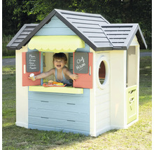 Kind spielt in einem bunten Spielhaus mit Fenster, Tür und Kreidetafel im Garten.