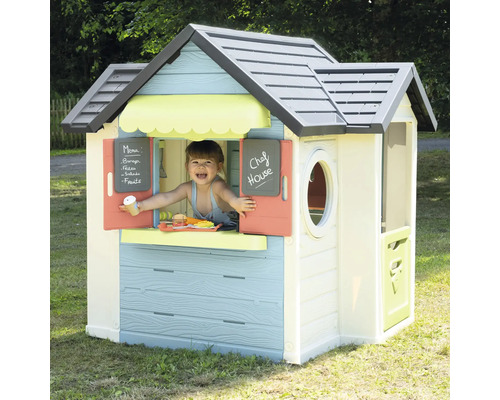 Kind spielt in einem bunten Spielhaus mit Fenster, Tür und Kreidetafel im Garten.