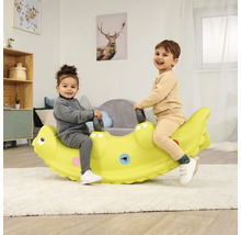 Zwei Kinder sitzen auf einer grünen Krokodilwippe in einem hellen Raum.
