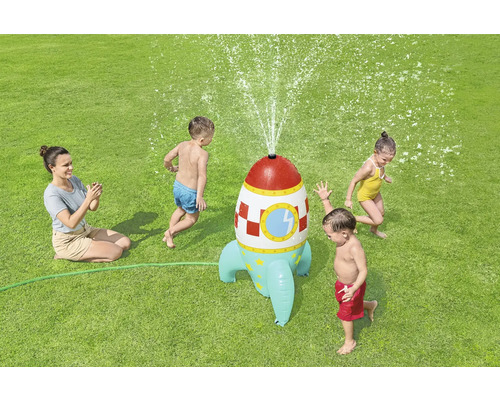Aufblasbare Raketensprenger mit spielenden Kindern und einer Erwachsenen auf einer Rasenfläche