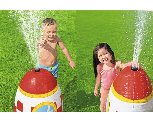Zwei Kinder spielen mit einer Wasserfontäne in Raketenform im Garten.
