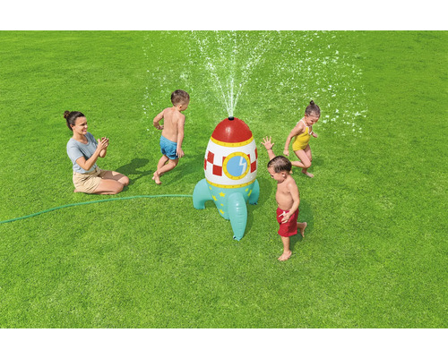Wassersprinkler in Raketenform mit spielenden Kindern auf einer Rasenfläche