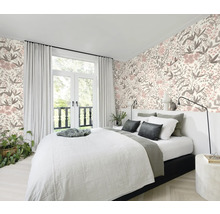 Schlafzimmer mit Bett vor einer floral gemusterten Tapete und einem Fenster mit Vorhängen.