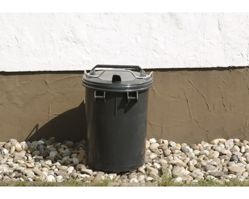 Grauer Abfallbehälter mit Deckel vor einer Hauswand auf Kies