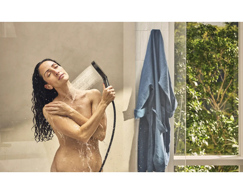 Frau unter der Dusche mit Handbrause und blauem Bademantel im Badezimmer