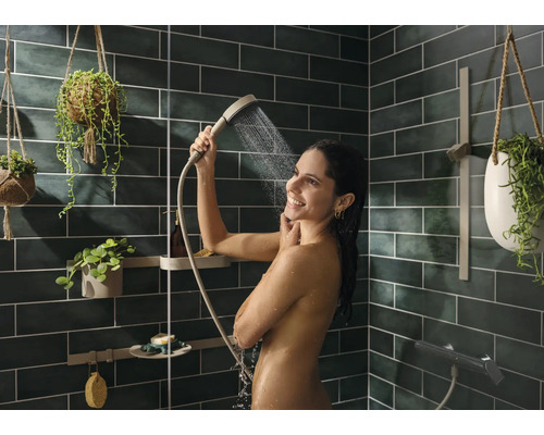 Frau unter der Dusche mit Handbrause in modernem Badezimmer mit grünen Fliesen und Hängepflanzen