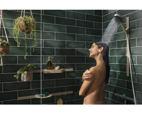 Frau unter der Dusche mit Duschkopf und grünen Fliesen im Badezimmer