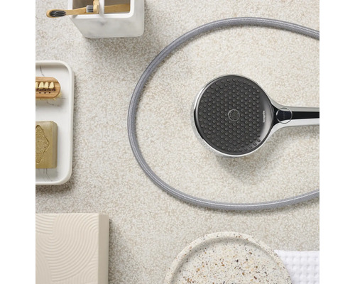 Handbrause mit Schlauch und Badezimmerutensilien auf hellem Hintergrund