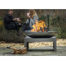 Feuerstelle im Garten mit brennendem Holz und zwei Personen im Hintergrund