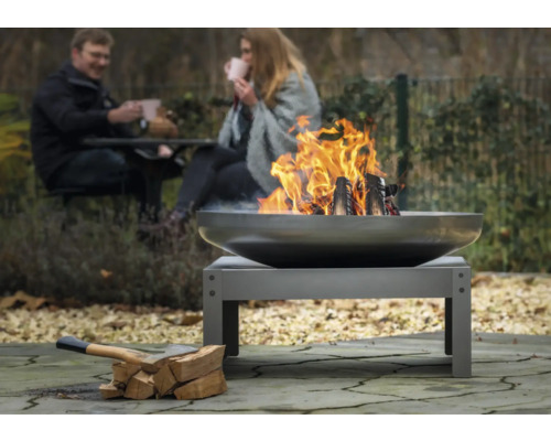 Feuerstelle im Garten mit brennendem Holz und zwei Personen im Hintergrund