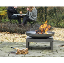 Feuerstelle im Garten mit brennendem Holz und Axt neben einem Holzstapel