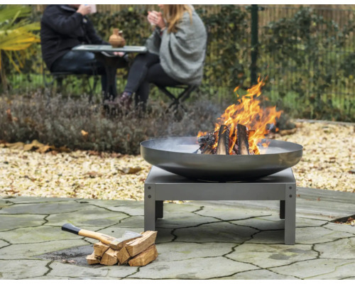 Feuerstelle im Garten mit brennendem Holz und Axt neben einem Holzstapel