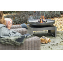 Feuerschale mit Holz auf einer Terrasse, daneben eine Person in einem Sessel